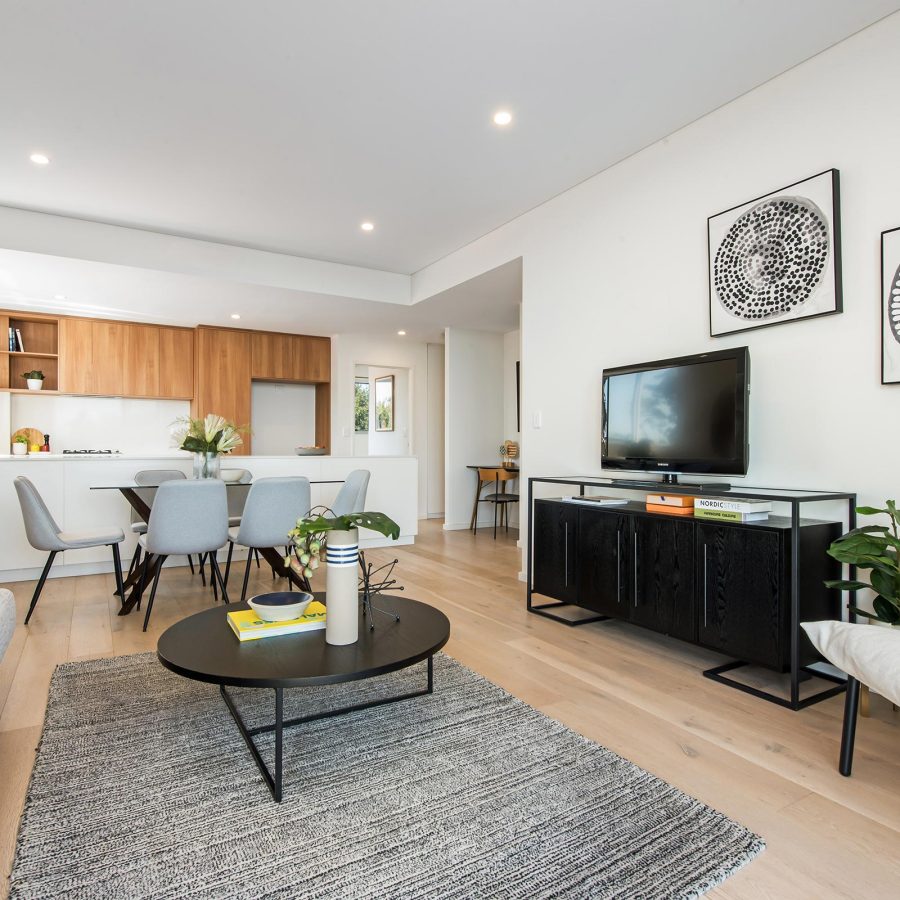 Open-plan living area with a grey sofa, round black coffee table, and a wall-mounted TV beneath two black-and-white circular art prints.